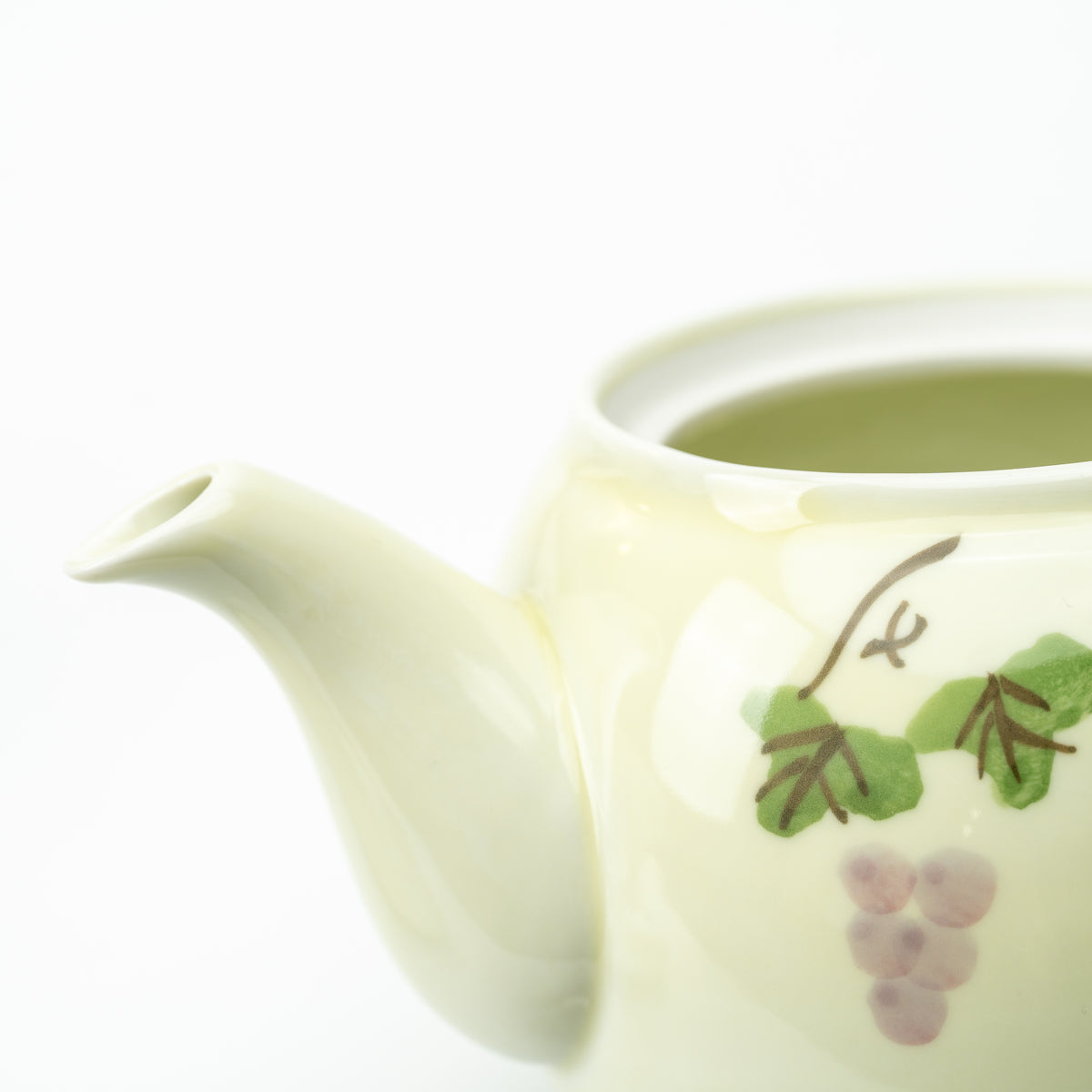 Detail of the grape-patterned teapot with its lid removed, showing the open mouth and curved spout.