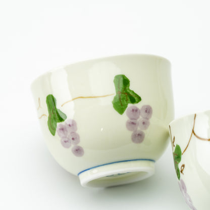Close-up of a matching Arita teacup with purple grapes, green leaves and a thin blue line around its foot.