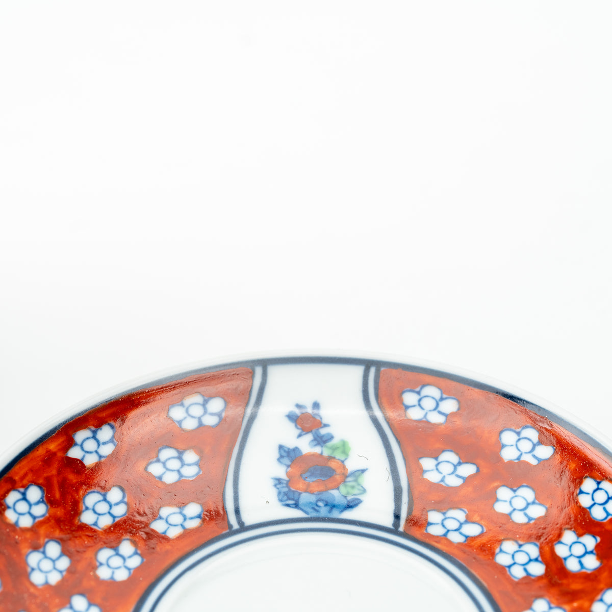 Detail of the Four Gentlemen saucer with an orange flower panel between red sections of small white blossoms.