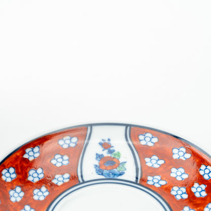 Detail of the Four Gentlemen saucer with an orange flower panel between red sections of small white blossoms.