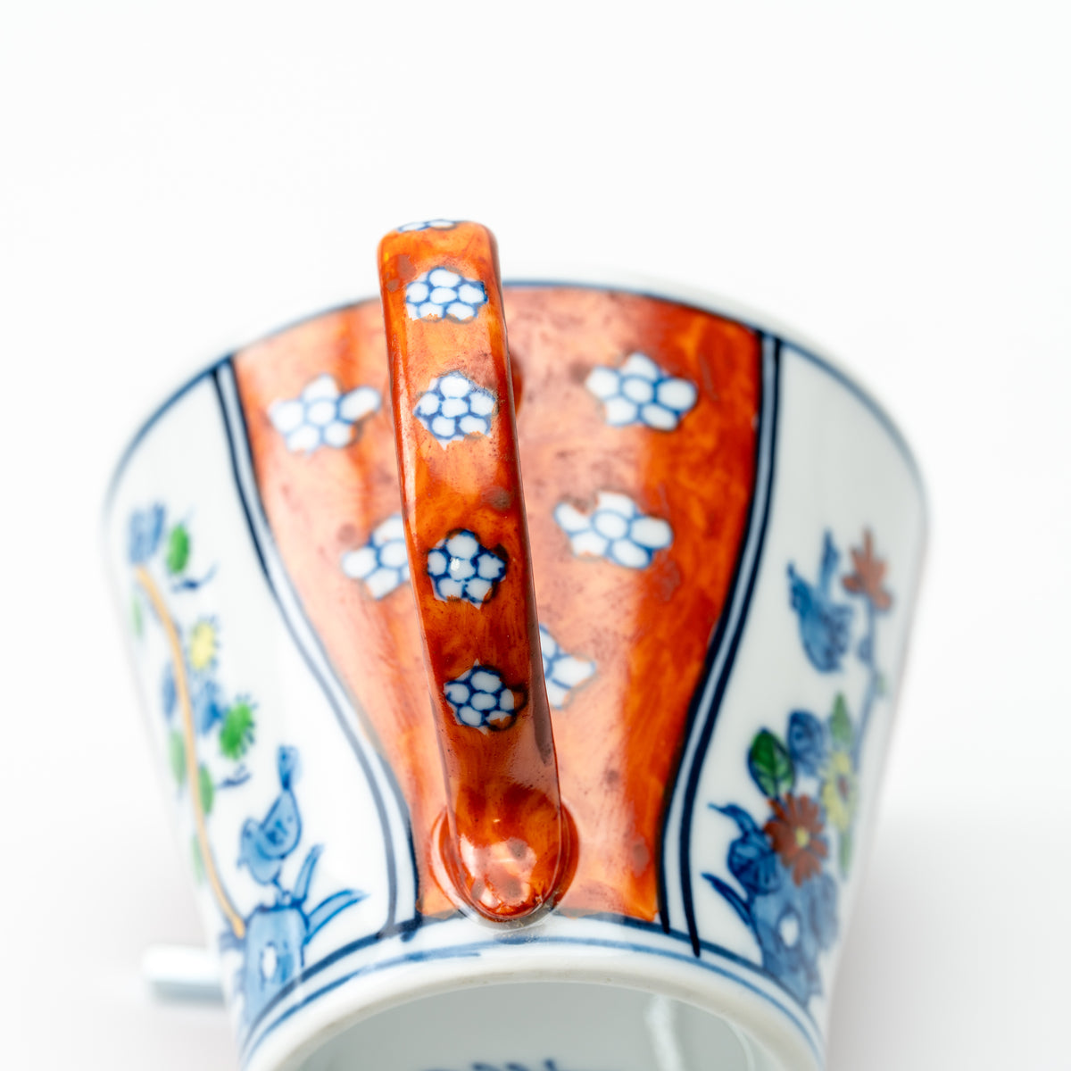 Handle-side detail of the Four Gentlemen cup, showing its red floral handle and alternating decorative panels.