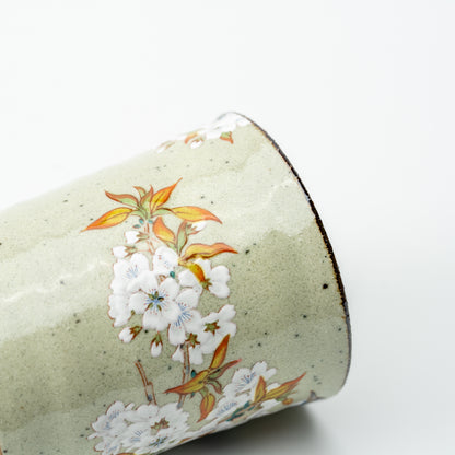 Detail of white cherry blossoms and orange-green leaves on the speckled pale green Kutani mug.