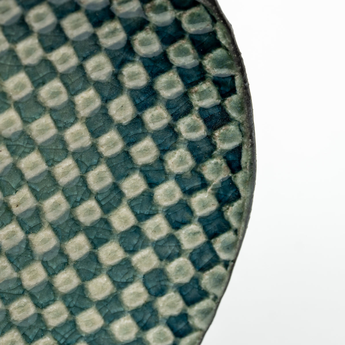 Close-up of raised pale squares against the dark teal surface of the Mosaic saucer.