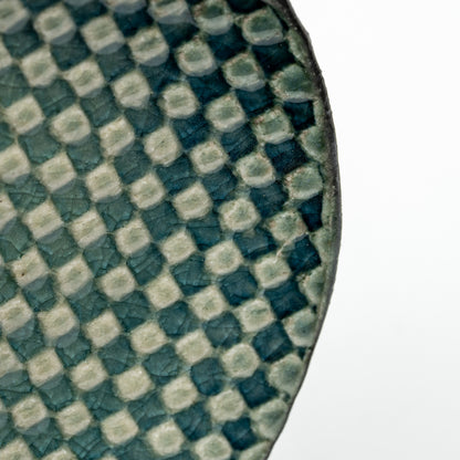 Close-up of raised pale squares against the dark teal surface of the Mosaic saucer.
