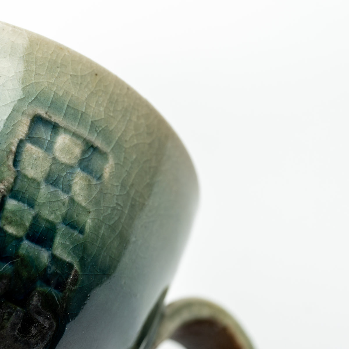 Detail of the Mosaic cup's checkered panel beneath its pale green rim, with part of the handle visible.