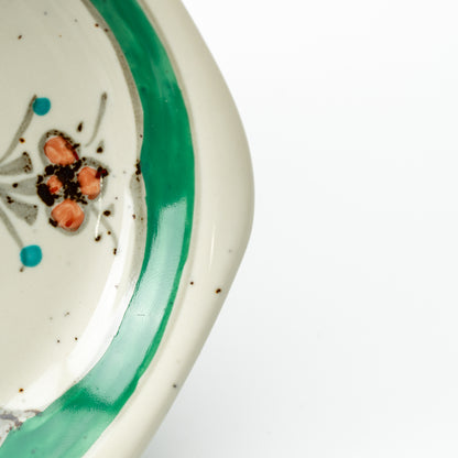 Close-up of the green border and orange flower on the hexagonal demitasse saucer.