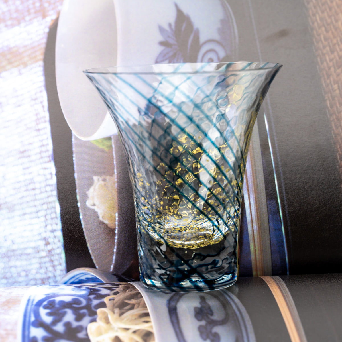 Blue-striped Yachiyo sake cup with gold-colored flecks displayed beside an open book.