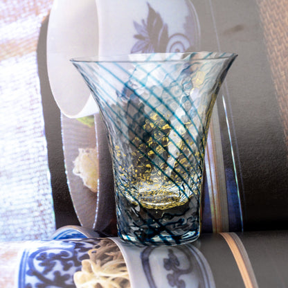 Blue-striped Yachiyo sake cup with gold-colored flecks displayed beside an open book.