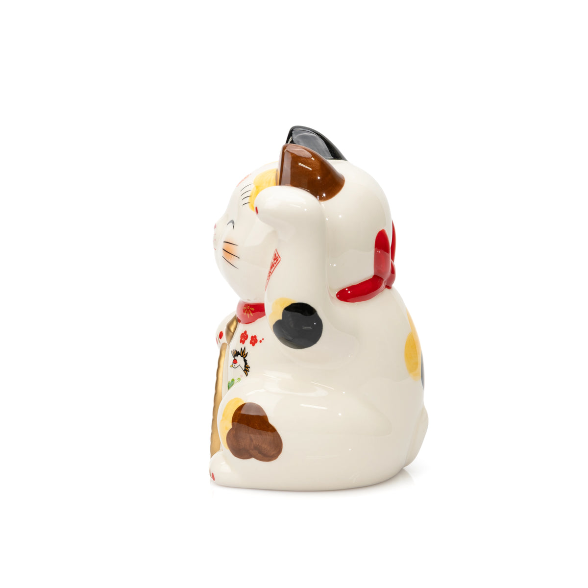 Side view of a Yakushigama lucky cat showing its raised paw, calico markings and red collar.