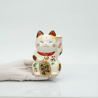Stationary calico lucky cat held in a gloved hand to show its size