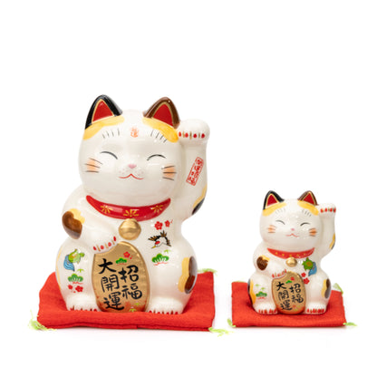 Large and small Yakushigama lucky cats side by side, each with one paw raised on a red cushion.