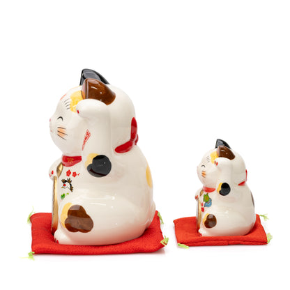 Side-by-side profile views of the large and small Yakushigama lucky cats on red cushions.