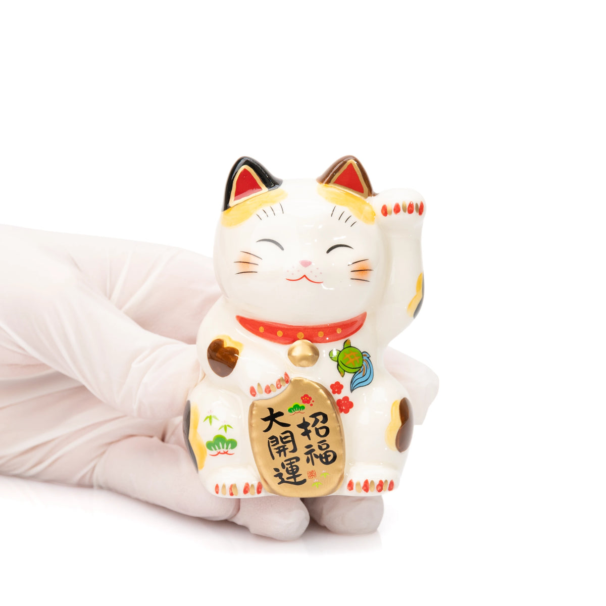 Small Yakushigama lucky cat held in a gloved hand for scale, showing its raised paw and gold-colored plaque.