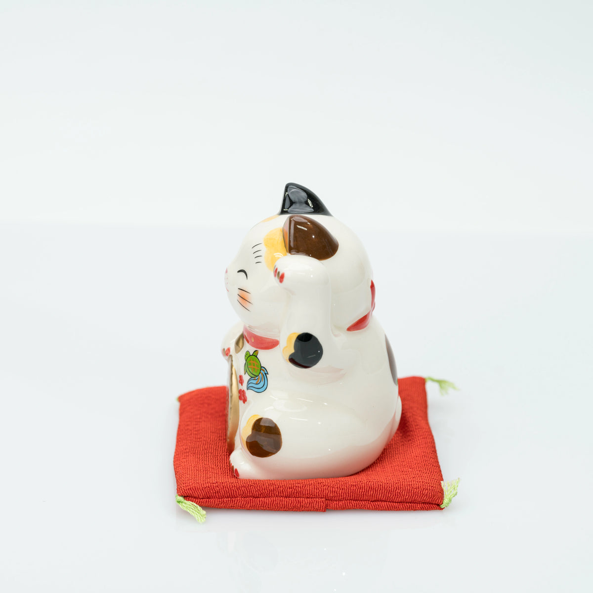 Side view of the stationary calico lucky cat on its cushion