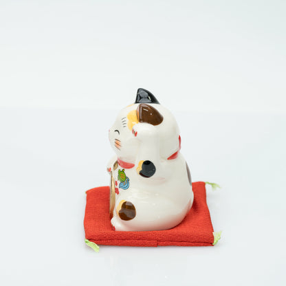 Side view of the stationary calico lucky cat on its cushion