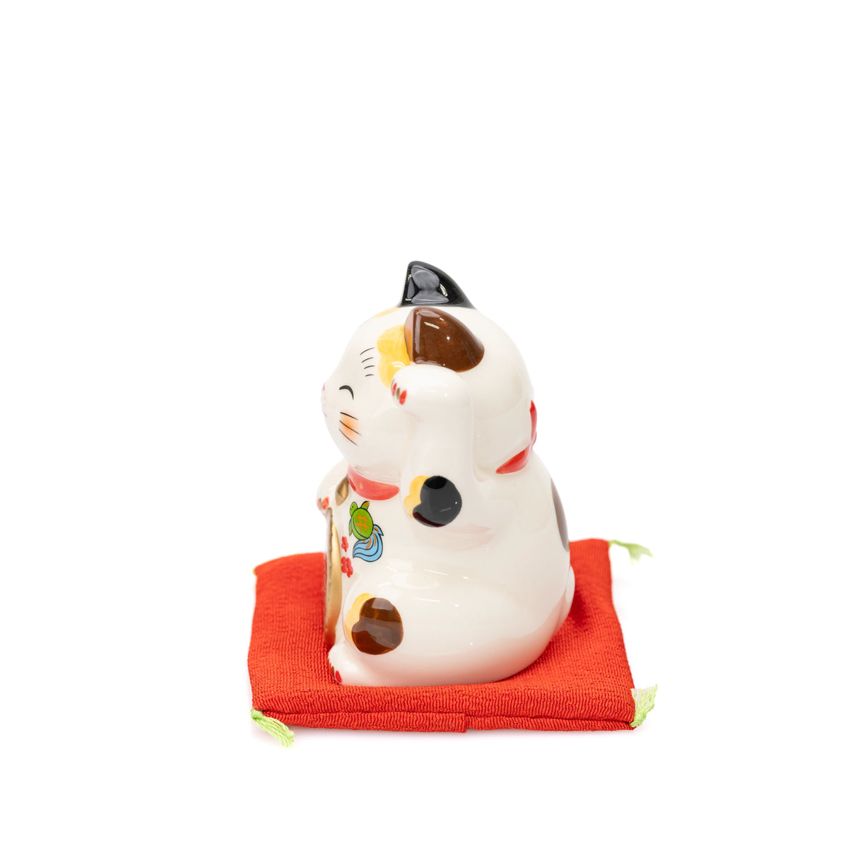 Side view of the small Yakushigama lucky cat on a red cushion, showing its calico markings.