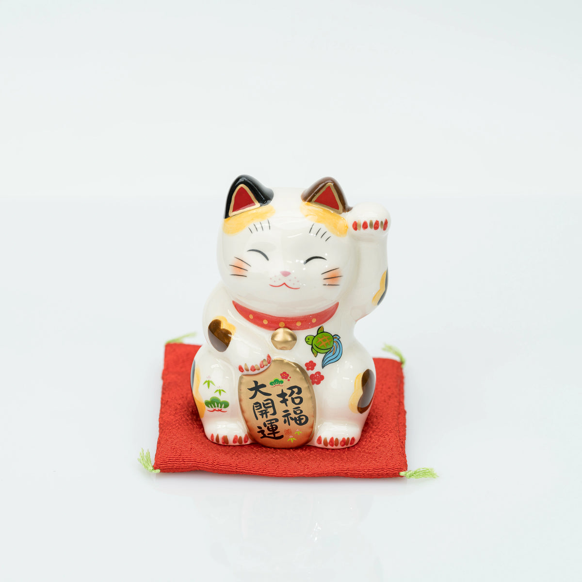 Front view of the stationary 15 cm calico lucky cat on its red cushion