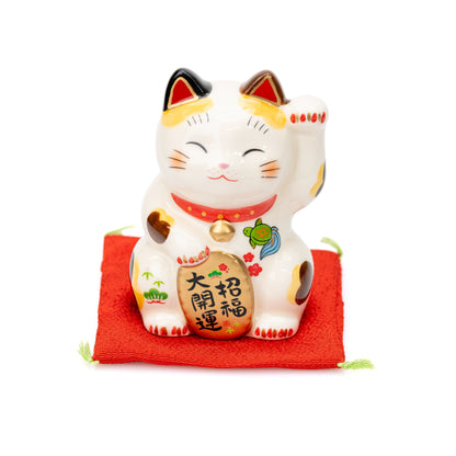 Angled front view of the small Yakushigama lucky cat on its red cushion.
