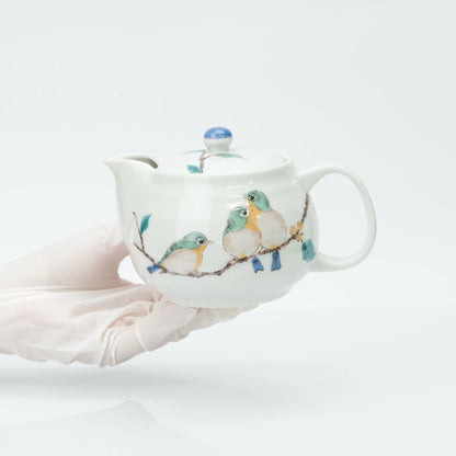 Gloved hands holding the 350 ml Kutani teapot from below, showing the rounded body, side spout and loop handle at scale.