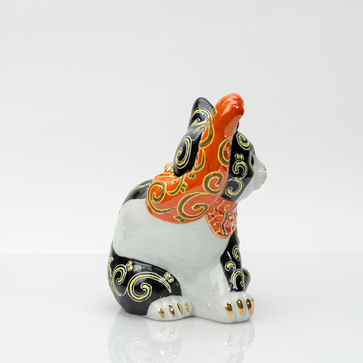Side view showing the white porcelain body, black markings and gold-tipped paws