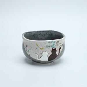 Grey Kutani matcha bowl with a white cat and a dark cat beneath blue flowers on the front