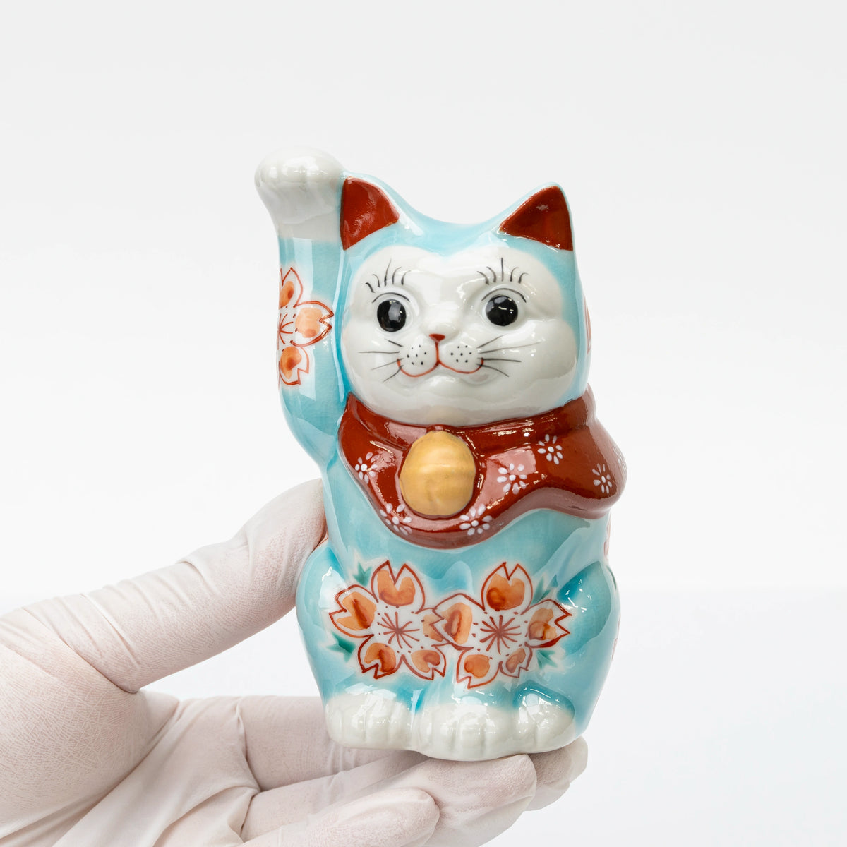 Turquoise blue lucky cat held in one hand to show its size, raised paw, and cherry blossoms