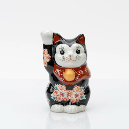 Front view of black maneki neko with a raised right paw, cherry blossoms, and a red bib