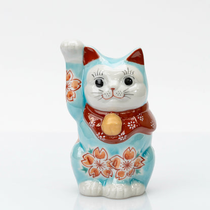Front view of turquoise blue Kutani lucky cat with cherry blossoms, a raised right paw, and a red bib