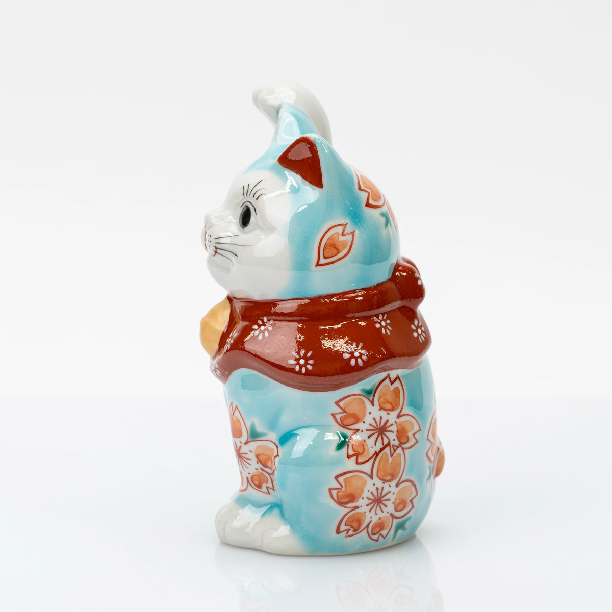 Side view of turquoise blue maneki neko with cherry blossoms and a red floral bib