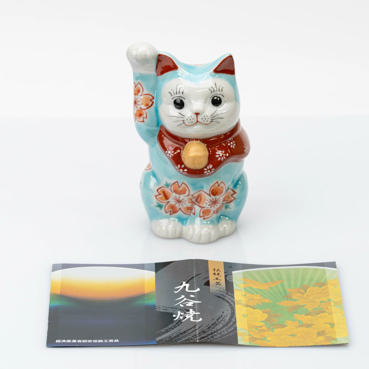Front view of turquoise blue Kutani lucky cat with a Kutani ware leaflet