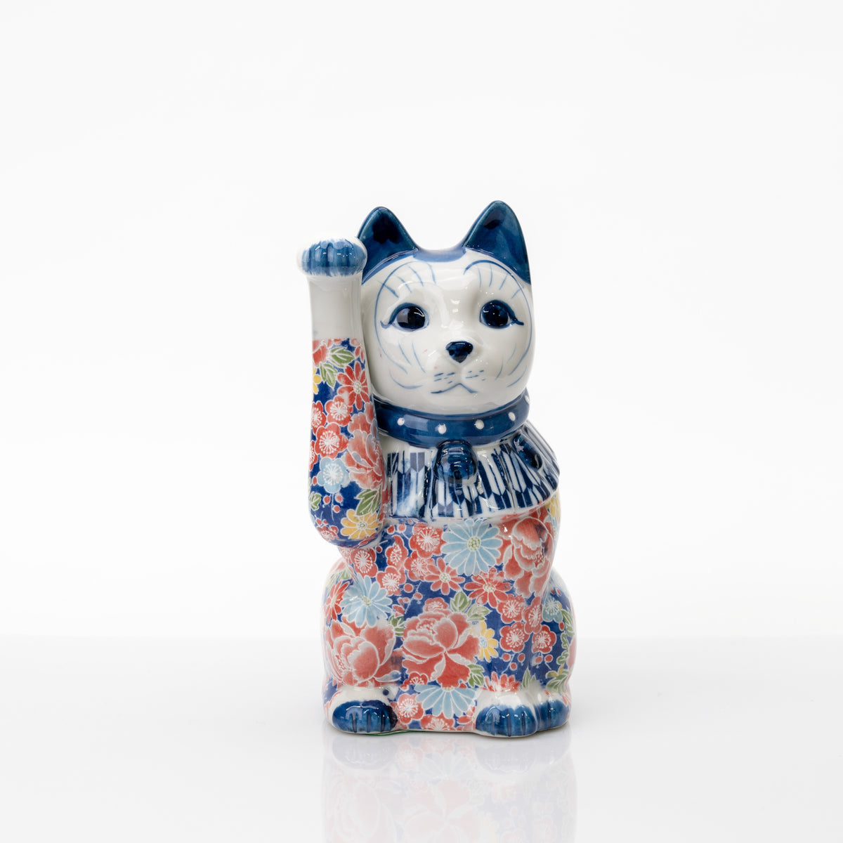 Chat porte-bonheur bleu à décor floral, montrant sa patte droite levée bien haut, son collier à pois et ses fleurs multicolores