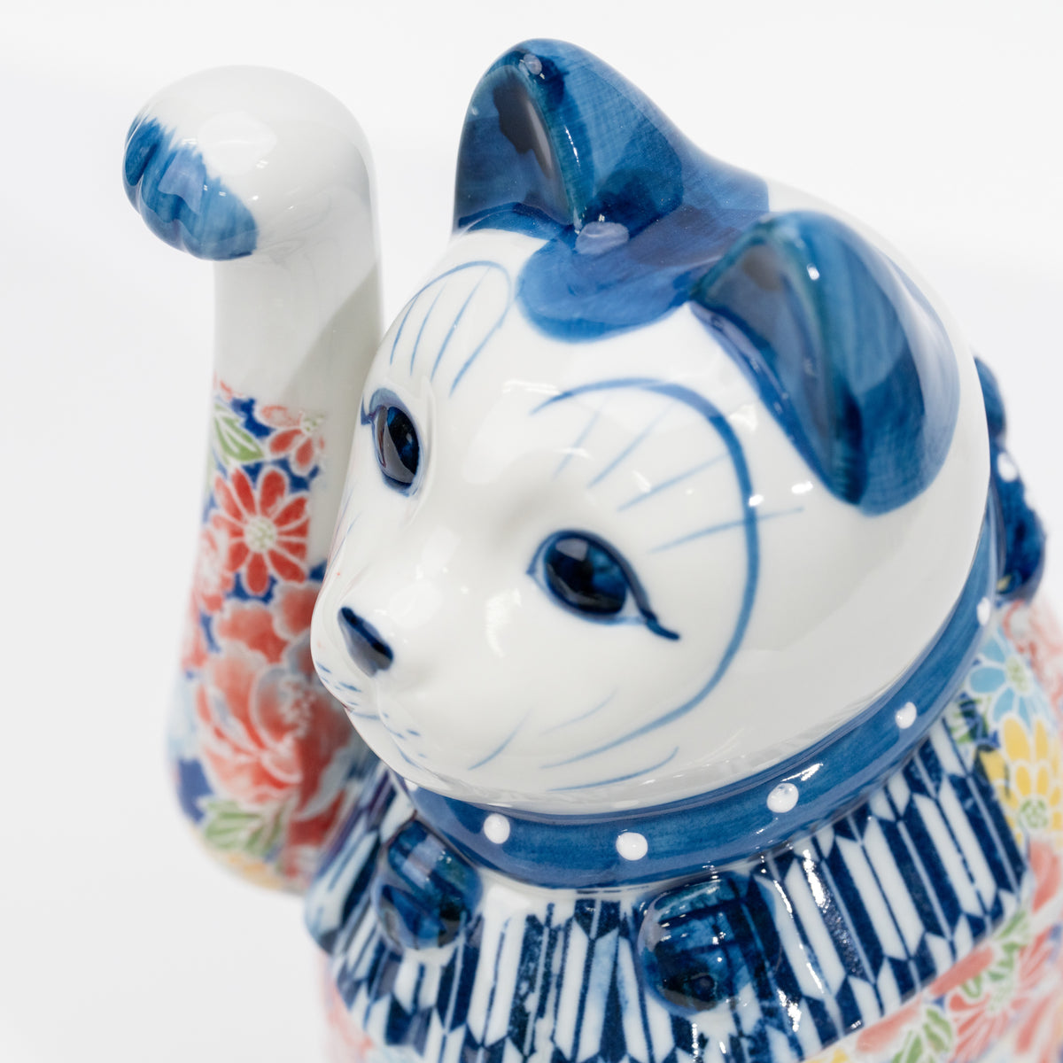 Gros plan sur le visage bleu et blanc, le collier et le détail de clochette moulée du chat porte-bonheur