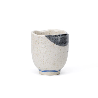 Back of the speckled cream yunomi, showing the dark gray rim accent and blue lines around the foot.