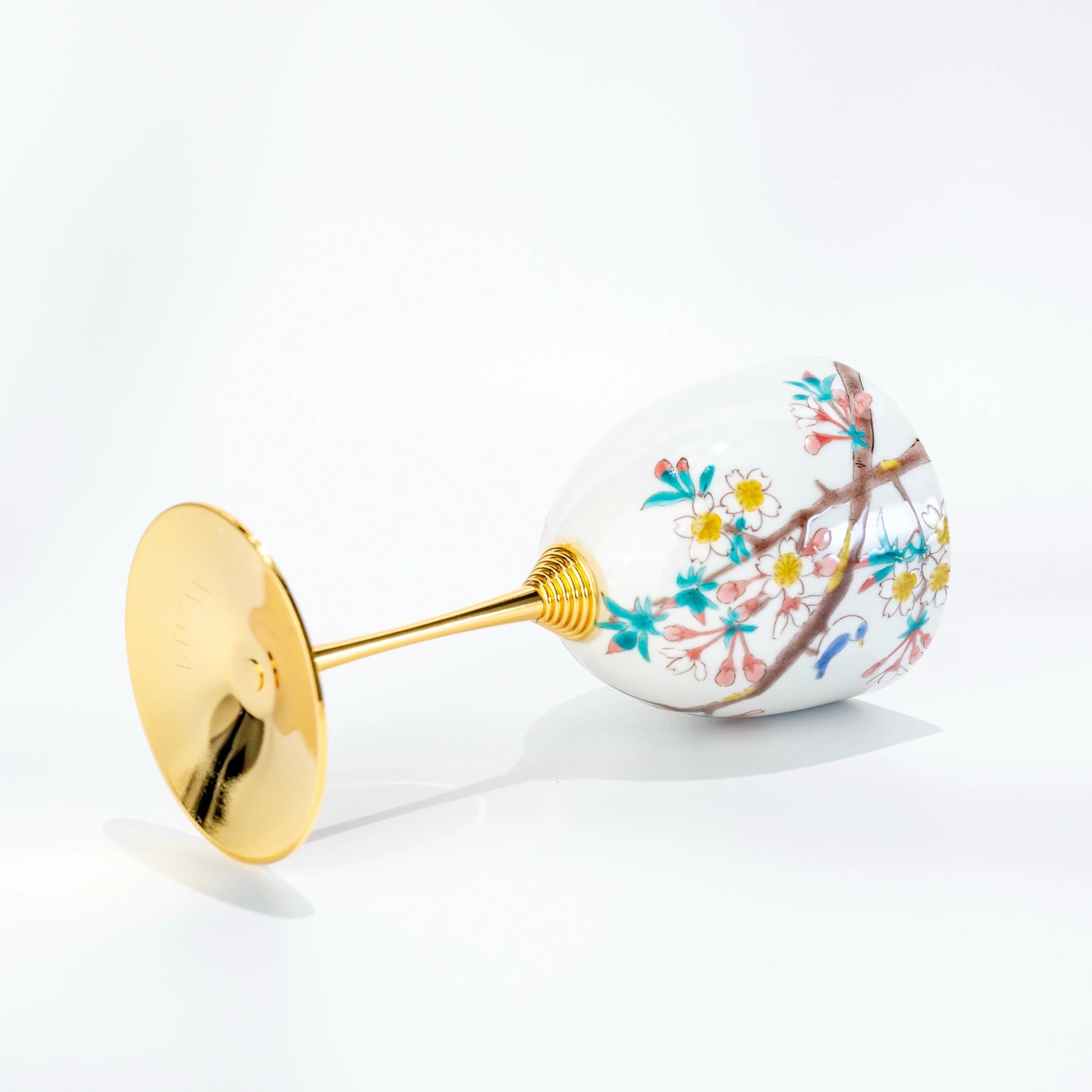 Side view of Kutani porcelain wine cup laid on its side with gold stem and painted bird motif