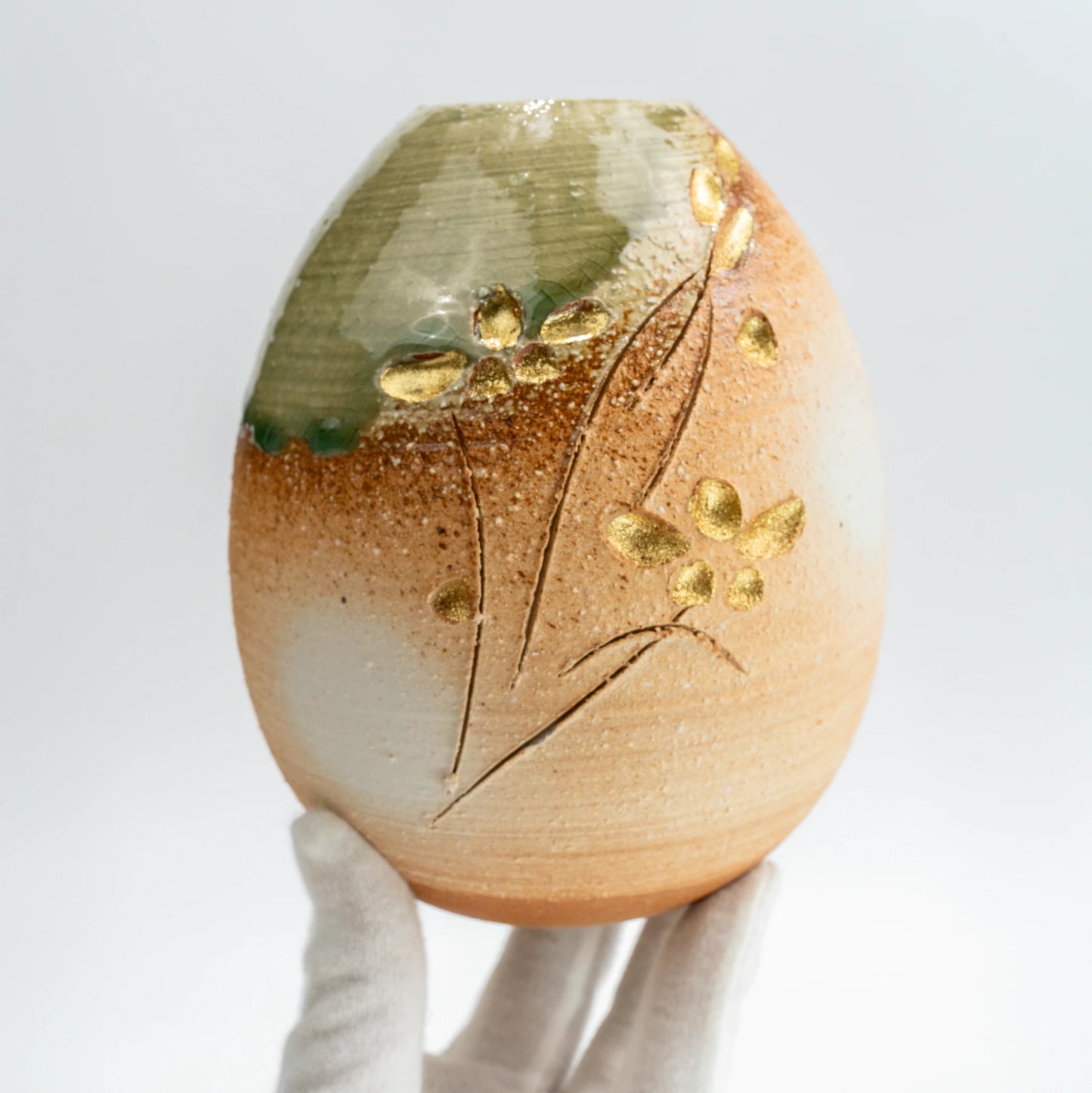 Handheld view of handmade Japanese pottery vase with green glaze
