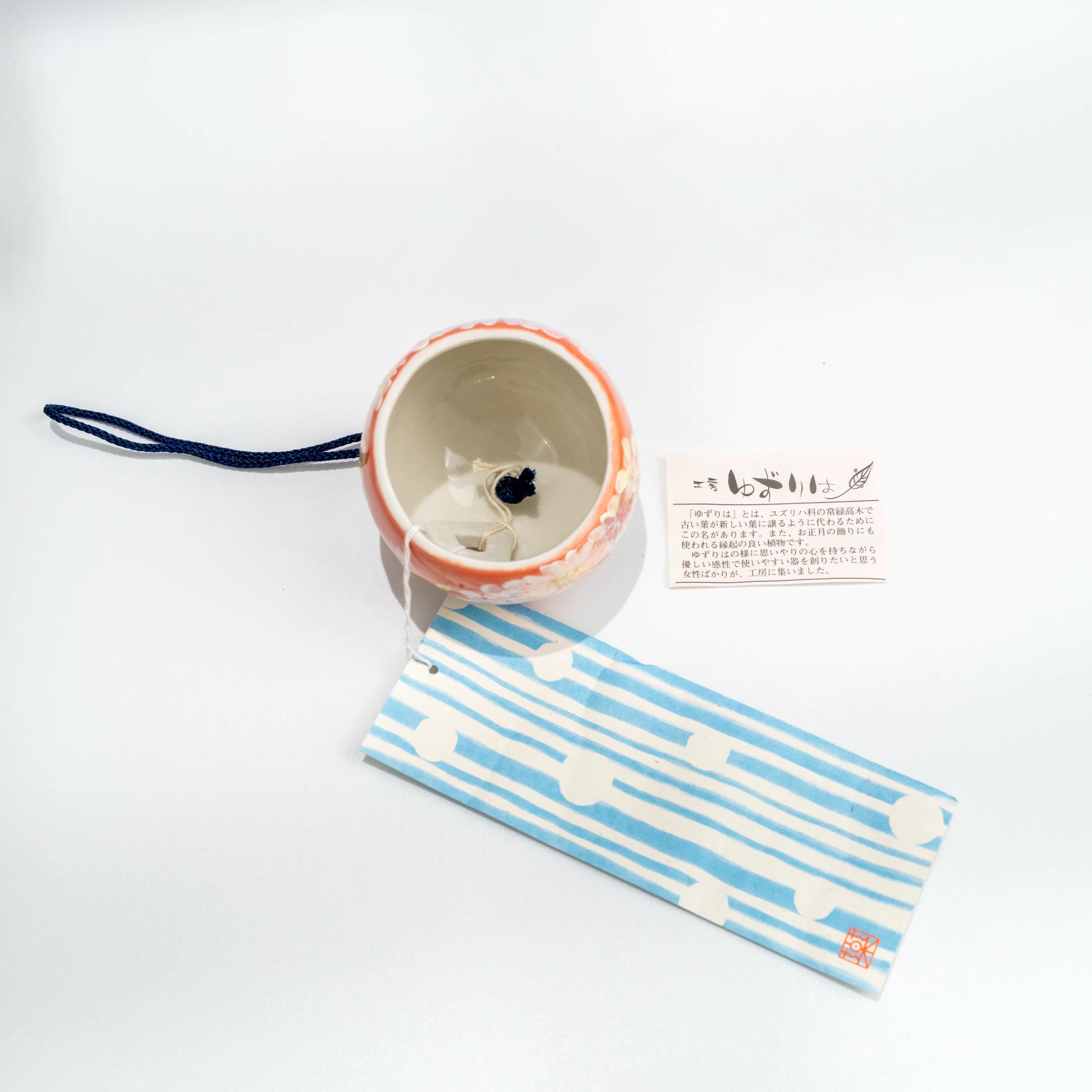 Top and underside view of floral ceramic wind chime with blue strip and tag
