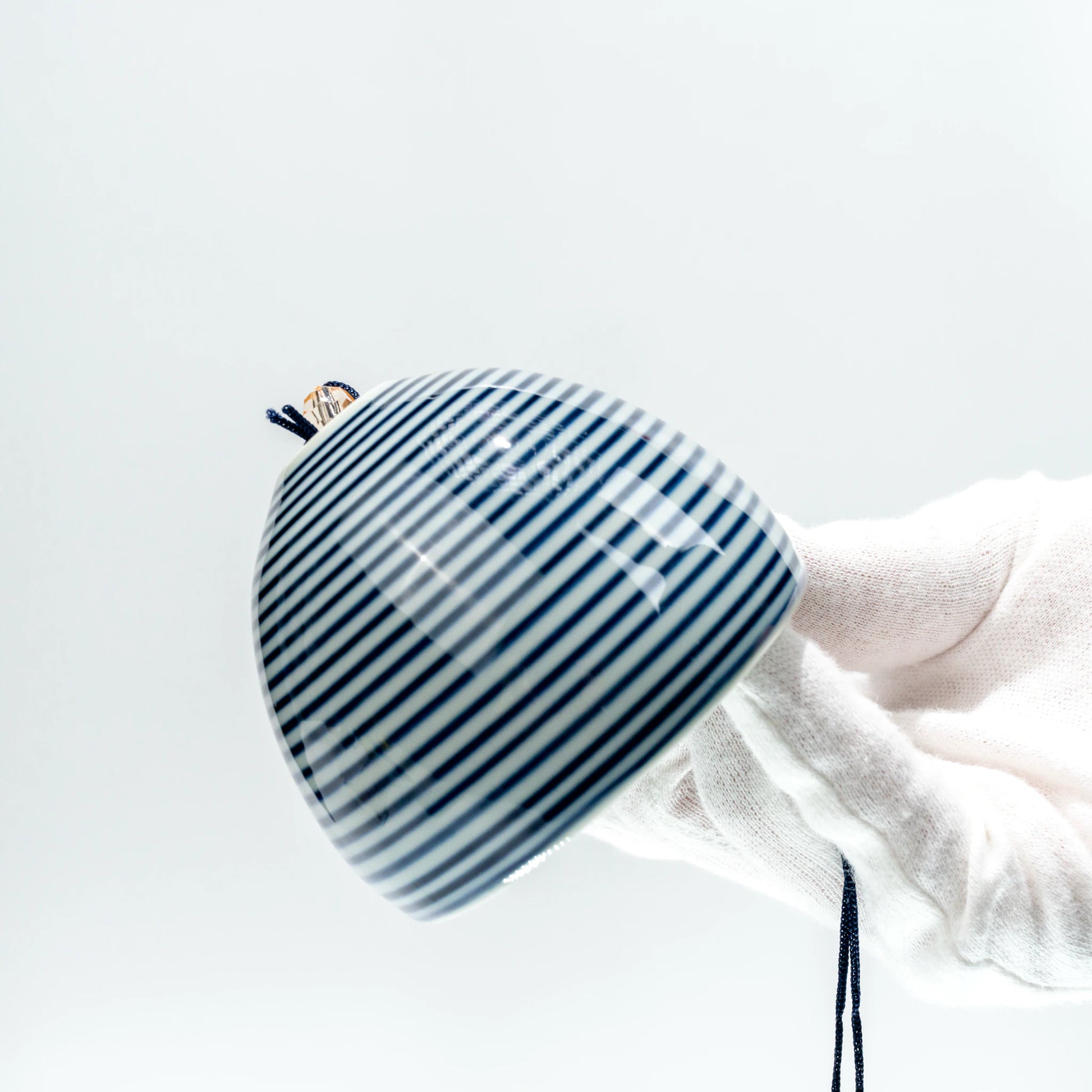 Angled side view of Japanese stripe ceramic furin bell held in hand