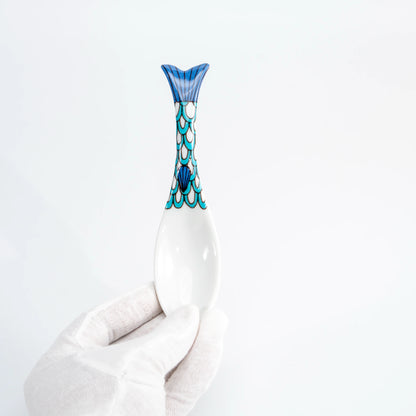 Hand-held blue Kutani whale renge spoon showing the whale-tail handle and white porcelain bowl