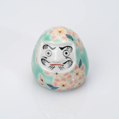 Angled front view of aqua Kutani Daruma with pink cherry blossoms