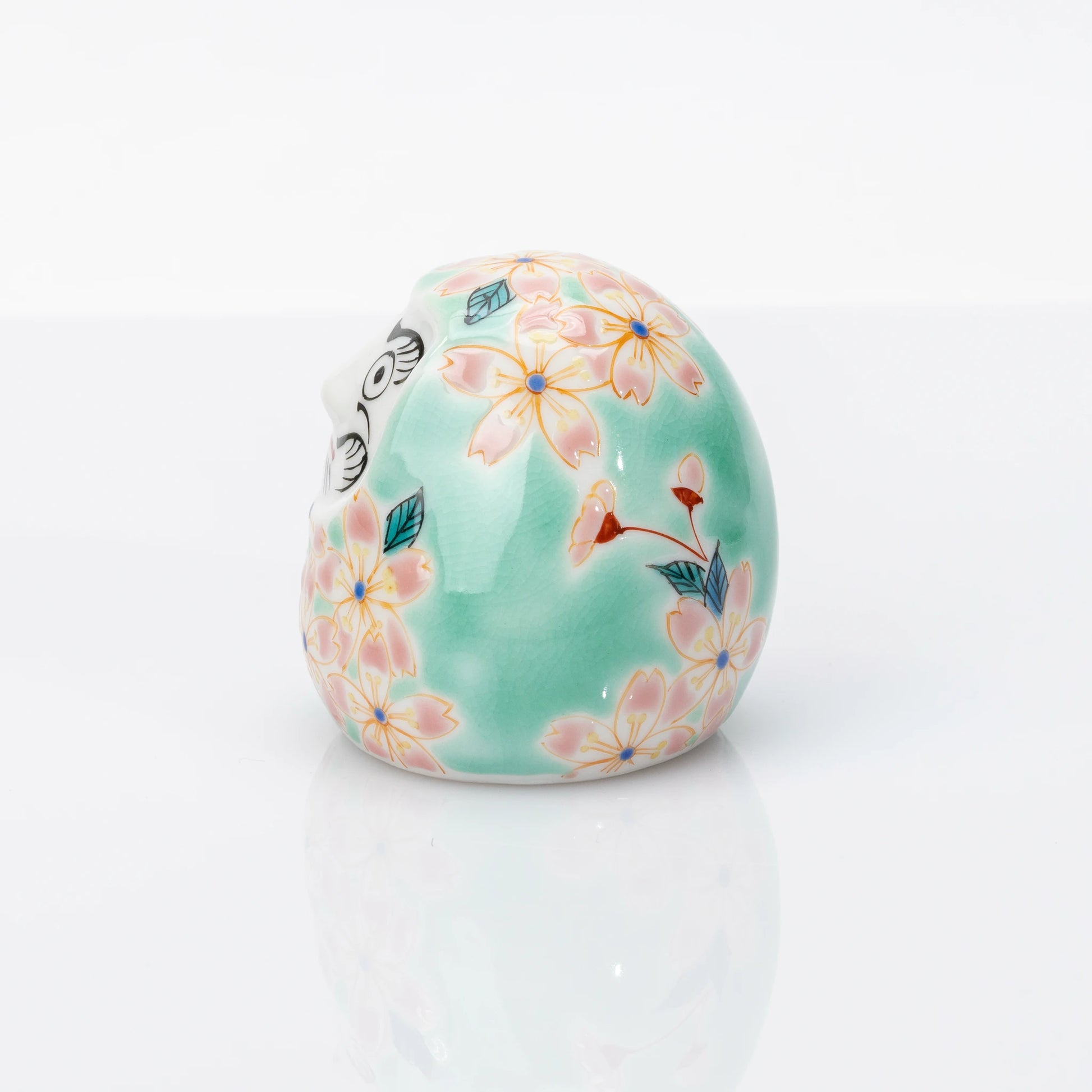 Side view of aqua Kutani Daruma with pink sakura decoration