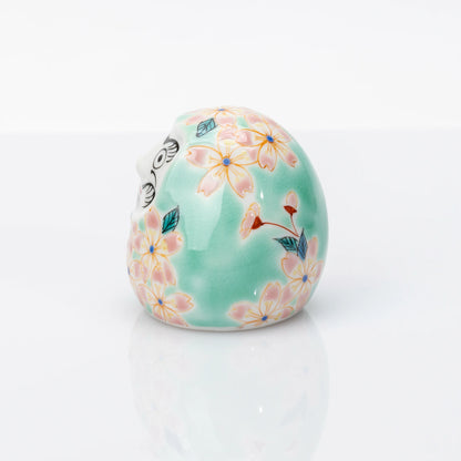 Side view of aqua Kutani Daruma with pink sakura decoration