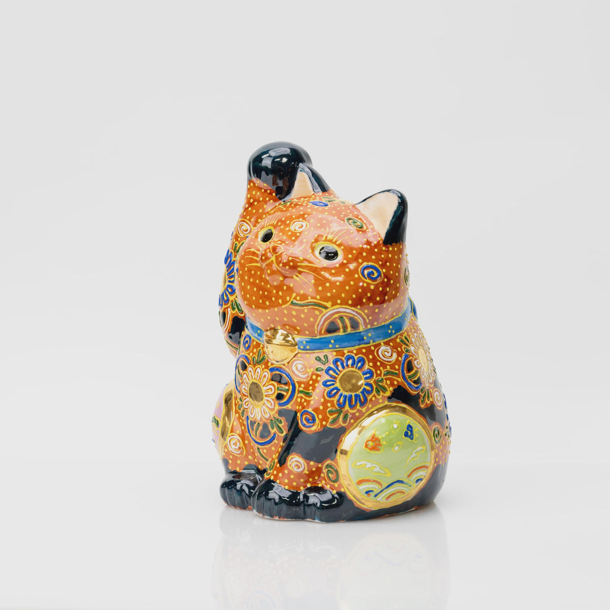 Three-quarter view of the porcelain lucky cat showing the light green side panel, blue collar, gold-tone bell and raised yellow dots.