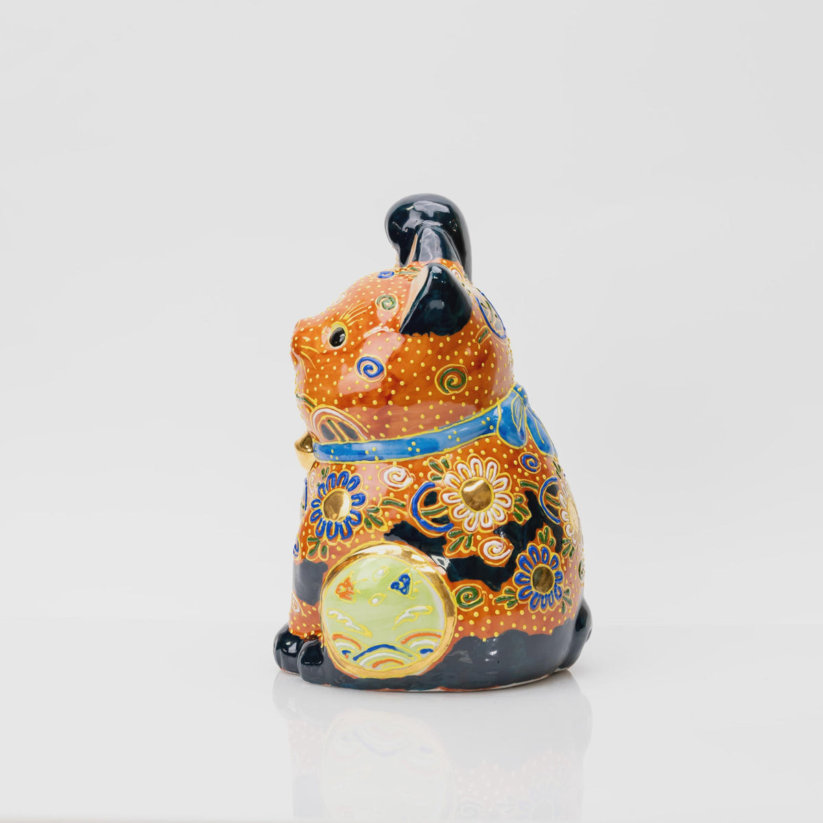 Side view of the Kutani lucky cat showing the light green circular panel, floral patterns and black glazed feet.