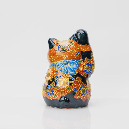 Side view of the Kutani lucky cat showing its raised right paw and pink circular panel with blue and green motifs.