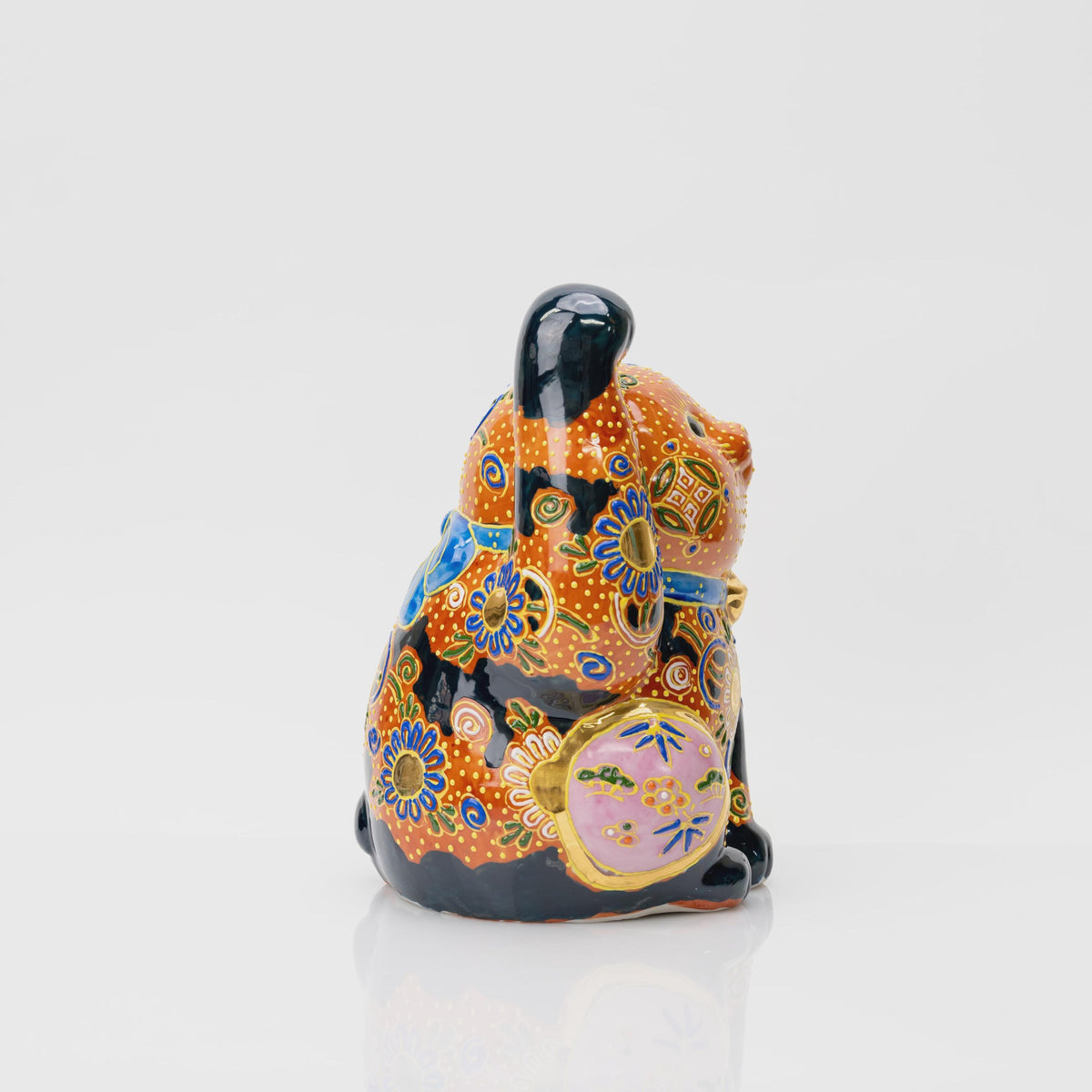 Rear view of the Kutani lucky cat showing a large blue collar bow, colorful flowers, yellow dots and a small curled black tail.