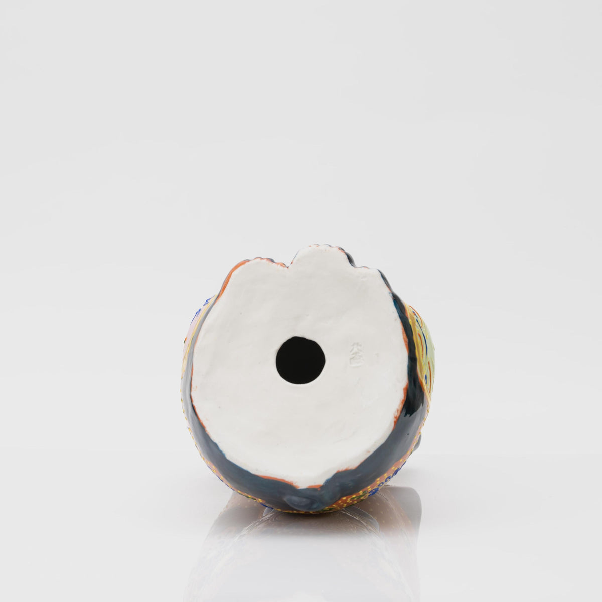 Underside of the porcelain lucky cat showing its pale unglazed base, central circular opening and small embossed mark.