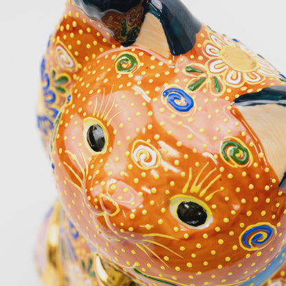 Close-up of the lucky cat's face with black eyes, yellow whiskers, raised yellow dots and blue, green and white spirals.