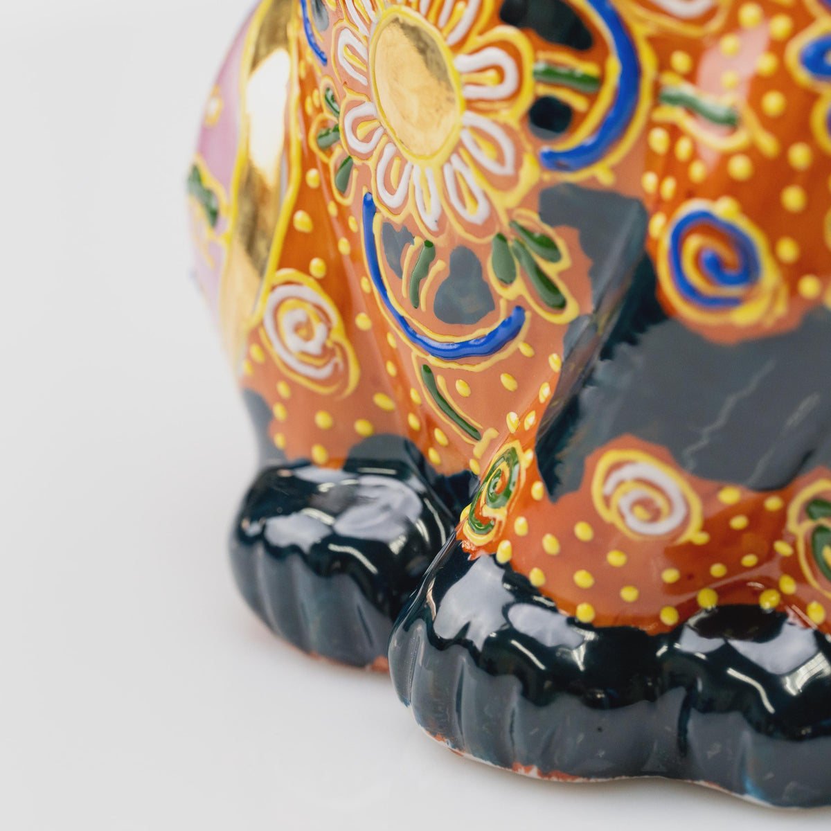 Close-up of the lucky cat's lower front showing glossy black paws, copper-orange glaze and raised floral decoration.
