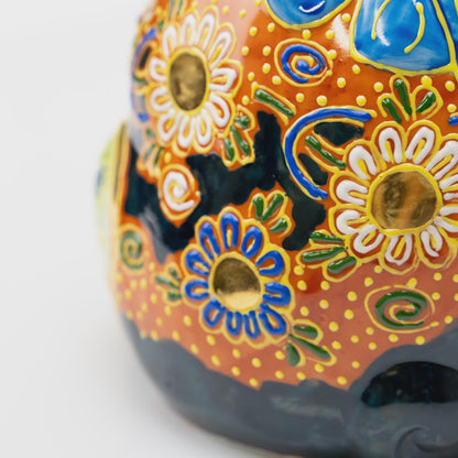 Close-up of blue and white floral decoration with gold-tone centers, green leaves and raised yellow dots on copper-orange glaze.