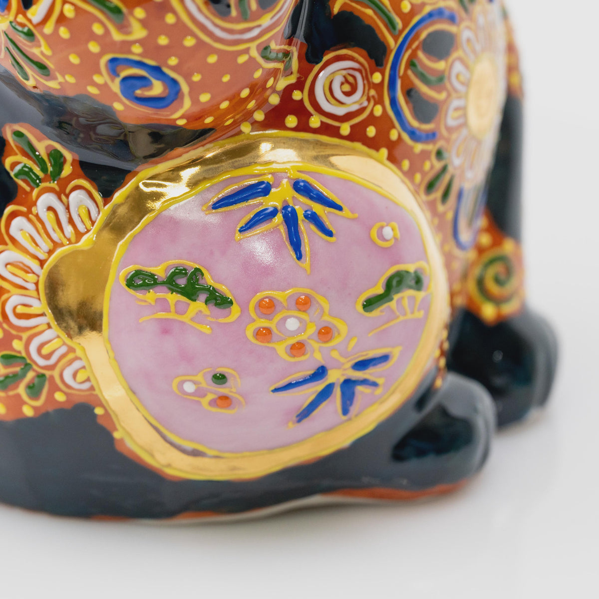 Close-up of the pink circular side panel with blue and green motifs, raised yellow outlines and a gold-tone border.